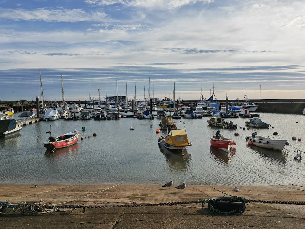 Boats moored in a calm harbor, with a cloudy sky and distant pier visible in Bridlington, Yorkshire.