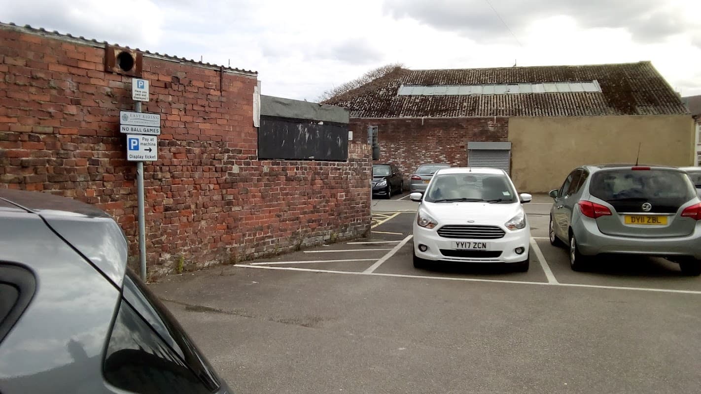 Brick wall with a parking sign, several parked cars, and a building with a corrugated roof in the background.