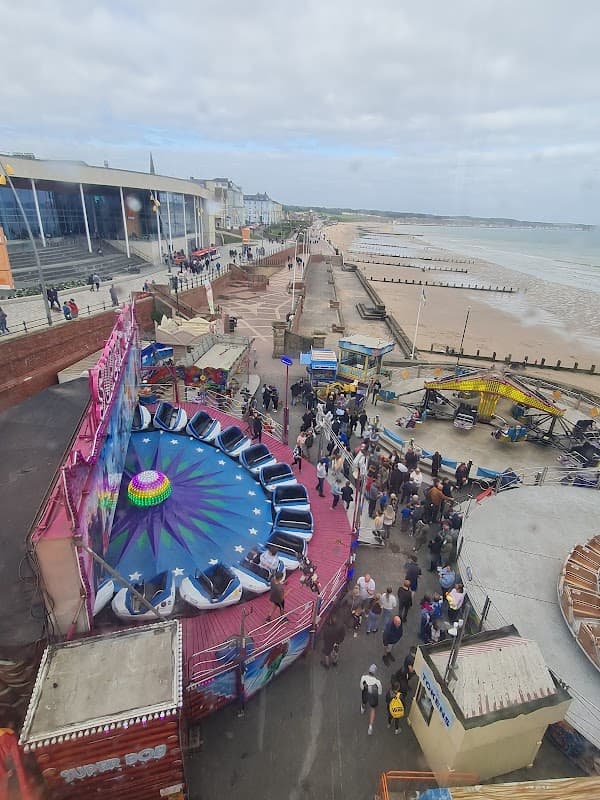 Pay & Display car park near a beach, with amusement rides and crowds enjoying the seaside in Bridlington, Yorkshire.