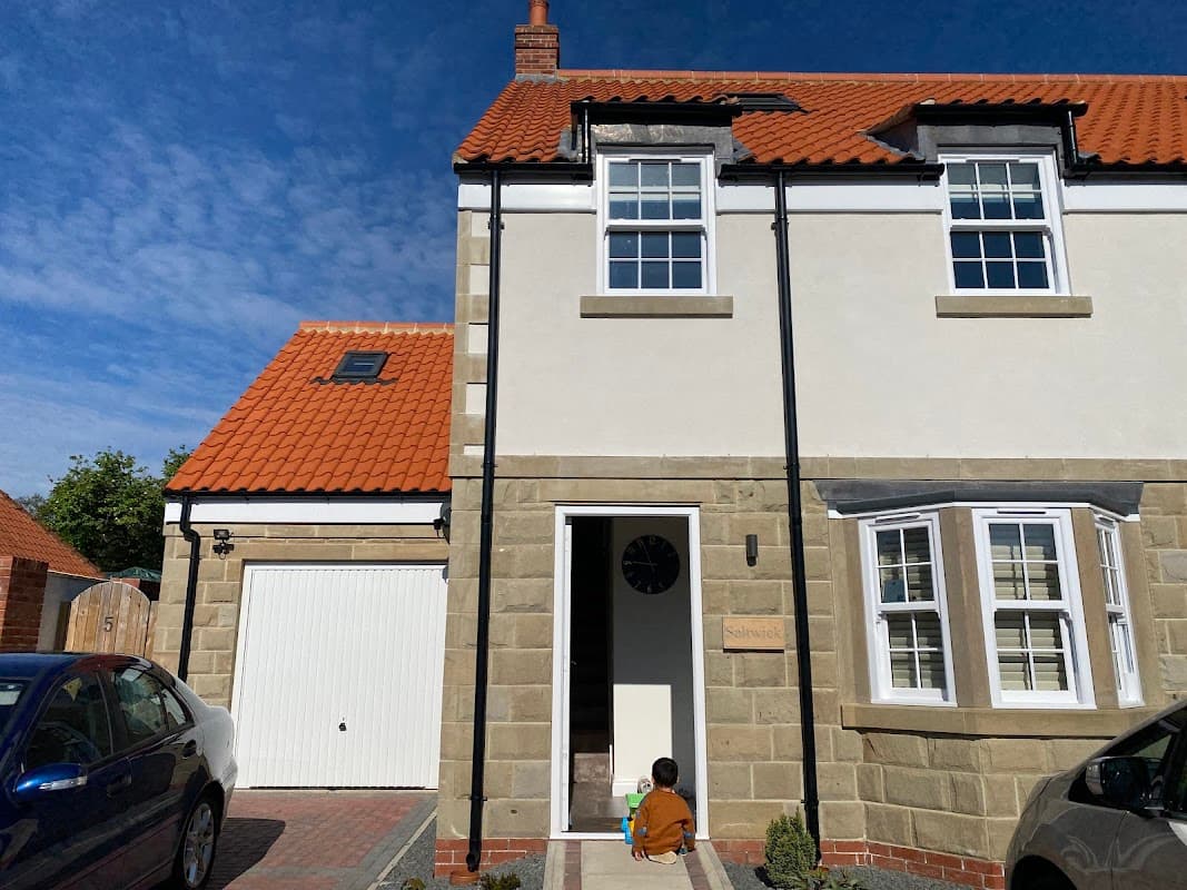 A two-story house with a red-tiled roof, a child sitting at the entrance, and a garage on the side.