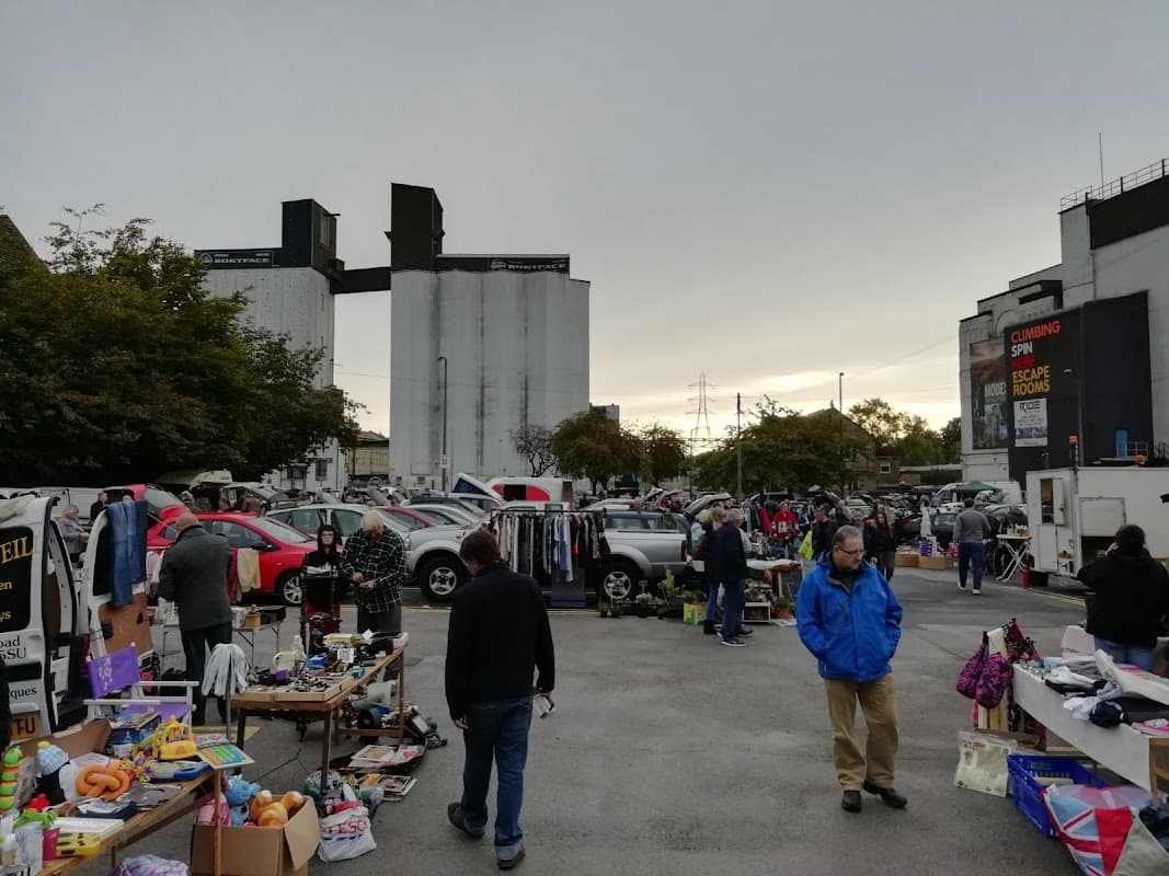 Busy car park market with stalls, shoppers, and parked cars under a gray sky in Brighouse, Yorkshire.