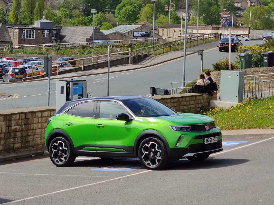 Bright green car parked in a Pay & Display lot, with buildings and trees in the background, and people sitting nearby.