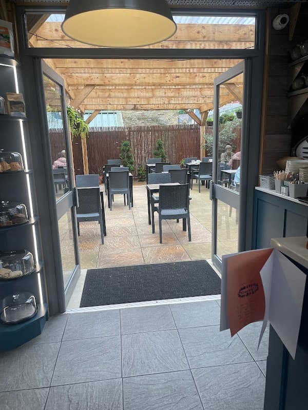 Open doors leading to a patio with tables and chairs, surrounded by greenery and a wooden pergola.
