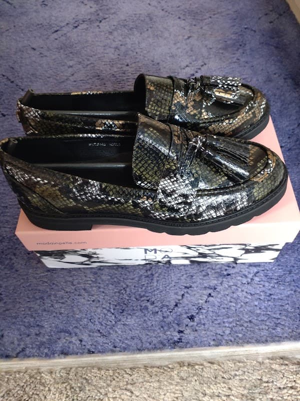 Stylish black and silver snake-print loafers on a pink shoe box, set against a plush purple background.