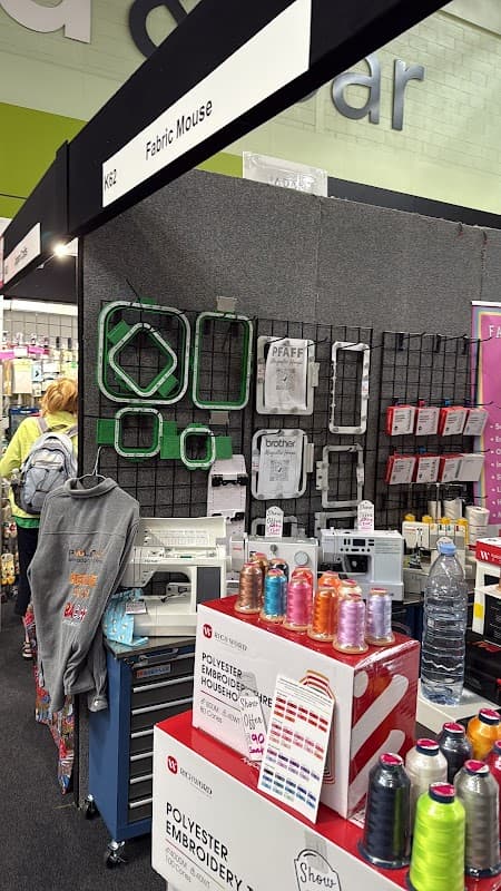 BAi Embroidery Machine display with colorful threads, embroidery hoops, and a grey hoodie on a stand at a trade show.