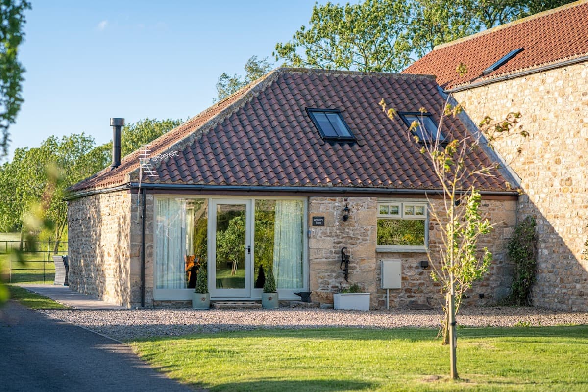 Charming stone building with a red-tiled roof, large windows, and a landscaped garden in Brompton-on-Swale, Yorkshire.