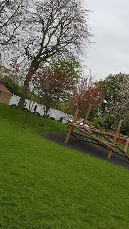 Playground equipment surrounded by trees and grassy area at Brompton-on-Swale Church of England Primary School.