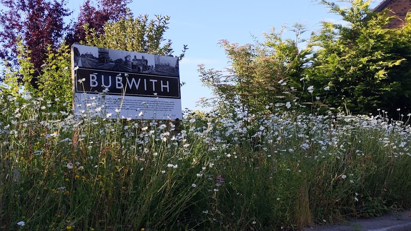 Sign for Bubwith surrounded by wildflowers and greenery under a clear blue sky.
