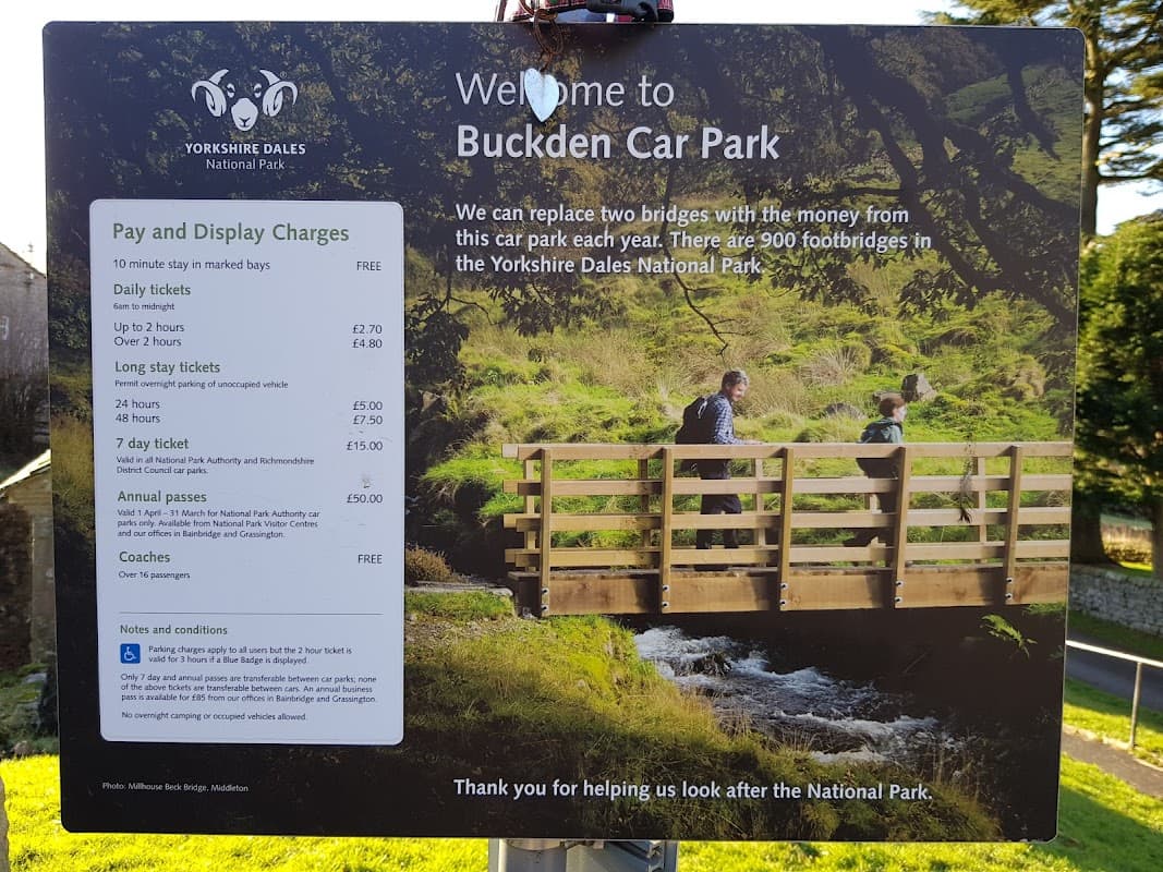 Welcome sign for Buckden Car Park, featuring a scenic bridge and information on parking fees and annual passes.