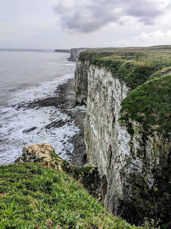 Dramatic cliffs at Bartlett Nab, overlooking the sea with grassy edges and waves crashing against the rocks below.