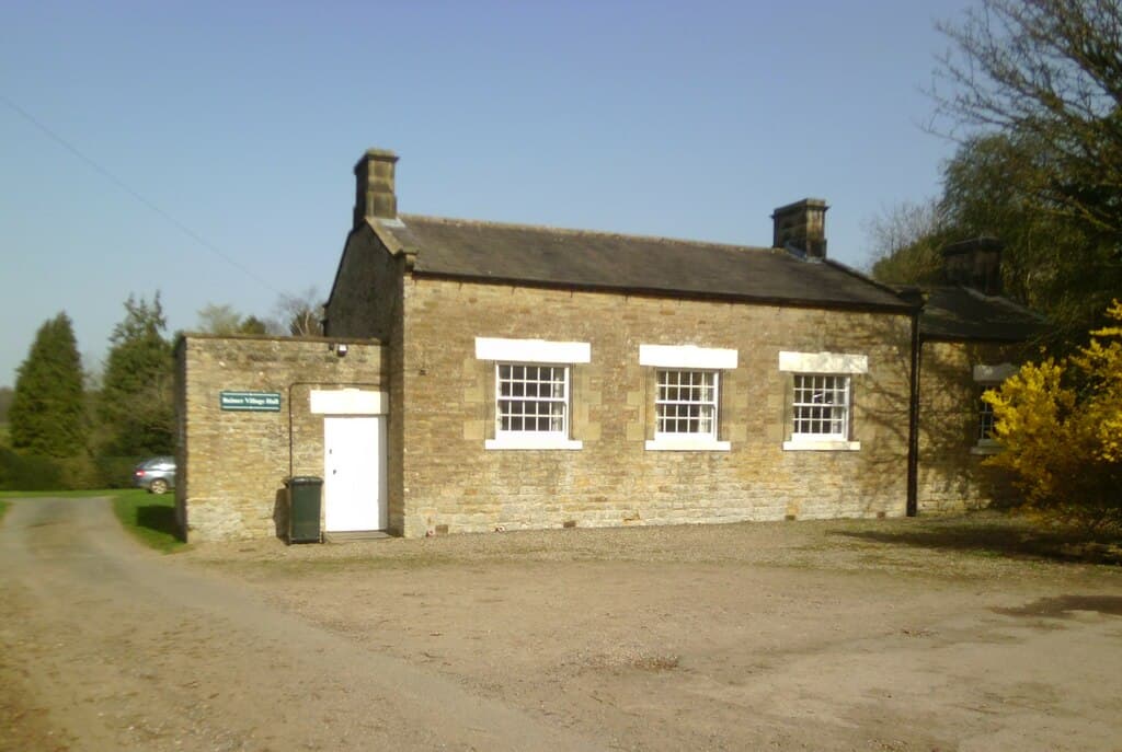 Stone building with white windows and door, surrounded by trees and gravel path in Bulmer, North Yorkshire.