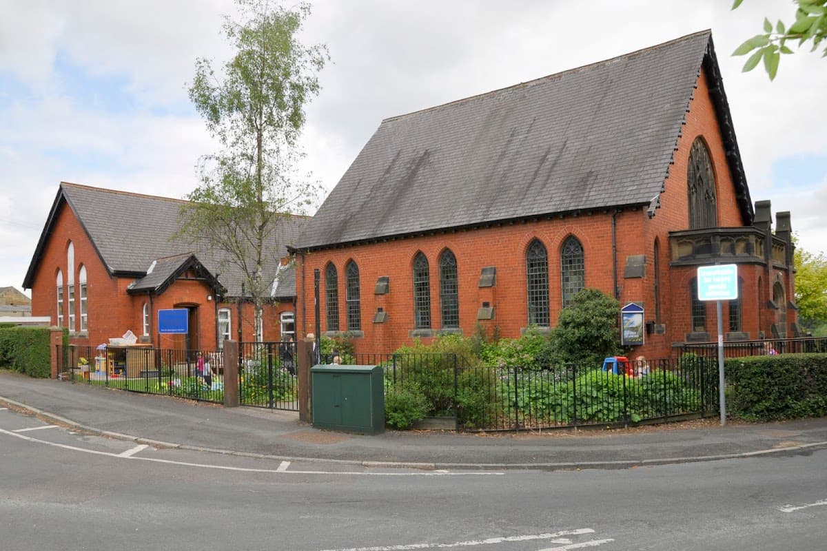 Red brick building with large windows, surrounded by greenery and a fence, located at a street corner in Burn Bridge.