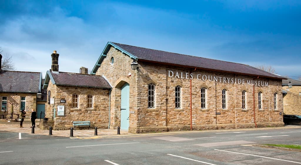 Historic stone building with large windows, sign reading "Dales Countryside Museum," and a person standing nearby.