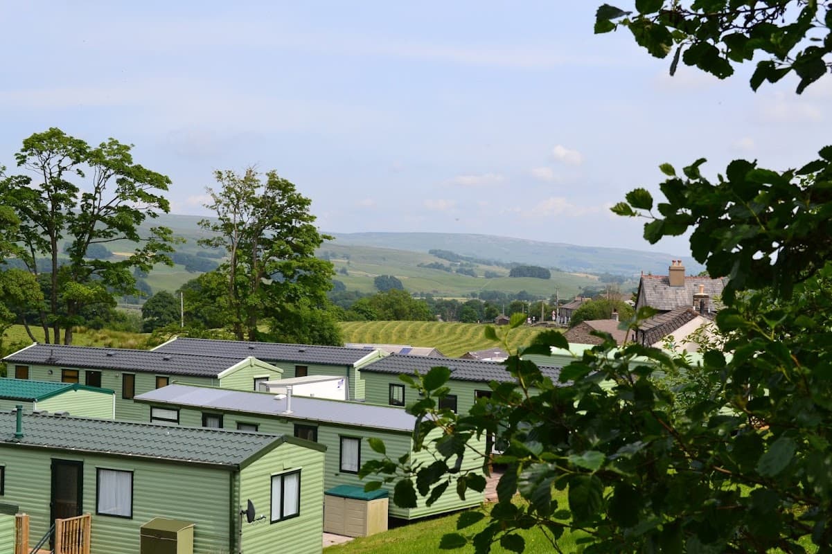 Green caravans nestled in a scenic landscape with rolling hills and trees in Burtersett, Yorkshire.