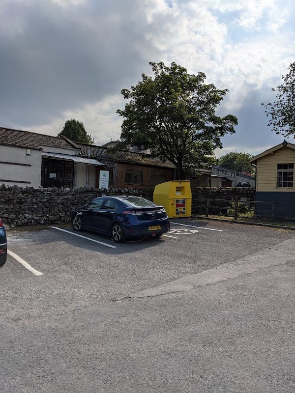 Pod Point charging station beside a parked car, with a stone wall and trees in the background in Burtersett, Yorkshire.