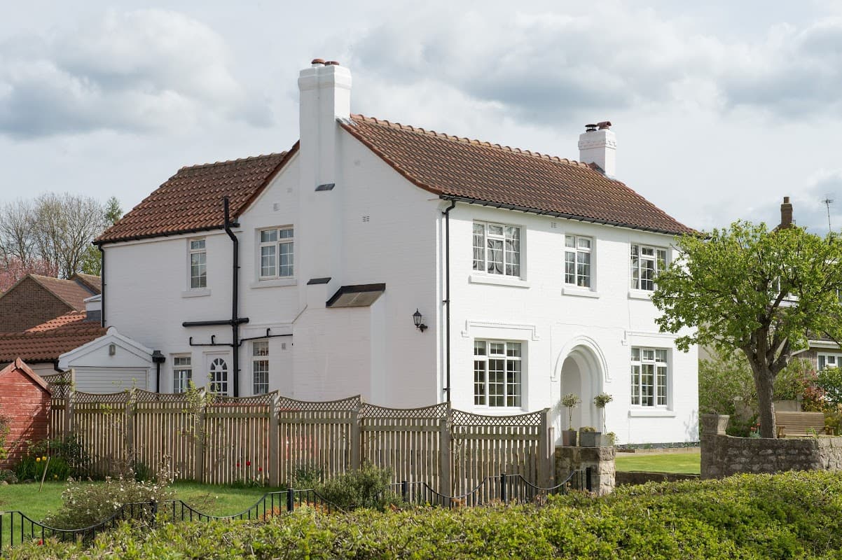White two-story house with a red tiled roof, surrounded by a wooden fence and greenery in Burton Leonard, Yorkshire.