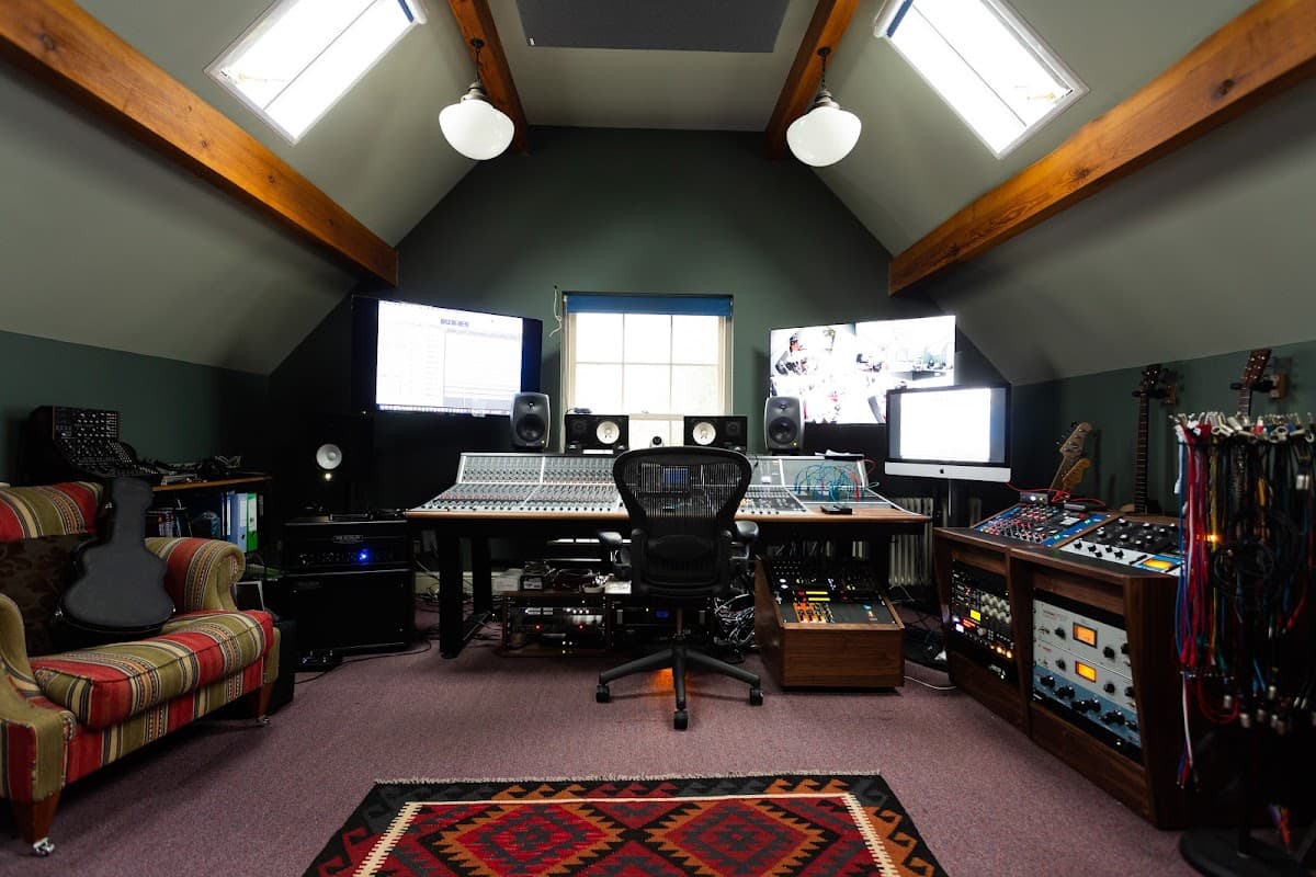 A cozy recording studio with large monitors, a mixing console, and various musical instruments on display.