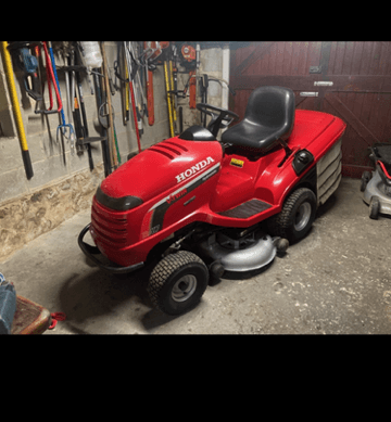 Red Honda lawn mower parked in a garage, surrounded by gardening tools on the wall.