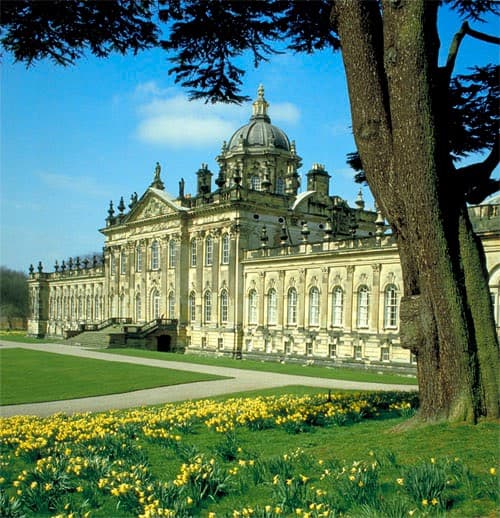 Historic building with ornate architecture, surrounded by lush greenery and blooming daffodils under a clear blue sky.