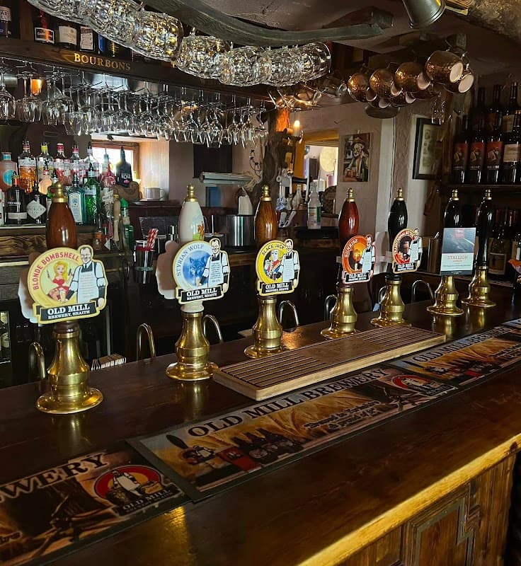Bar counter with various beer pumps, bottles, and glasses in a cozy pub setting.