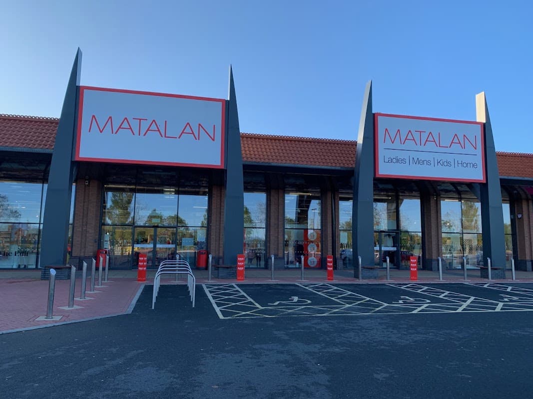 Matalan storefront with large signage, featuring sections for ladies, men, kids, and home. Clear blue sky above.