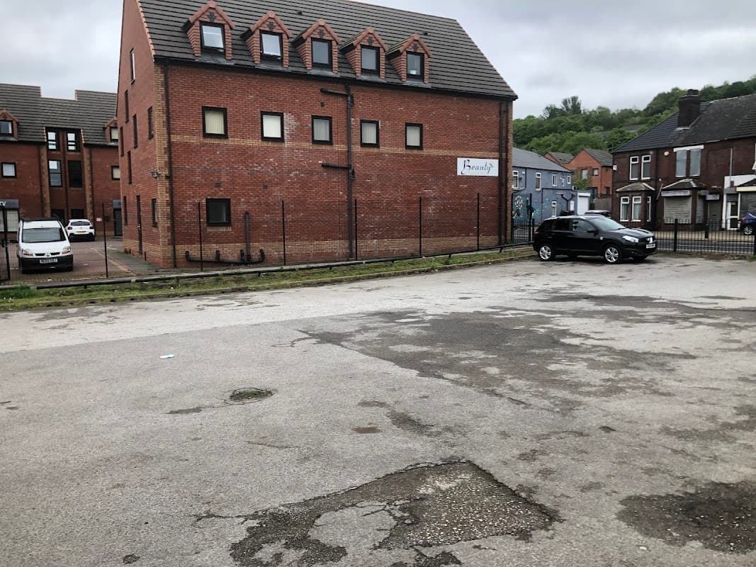 Free parking area with a gravel surface, surrounded by brick buildings and a few parked cars. Overcast sky.