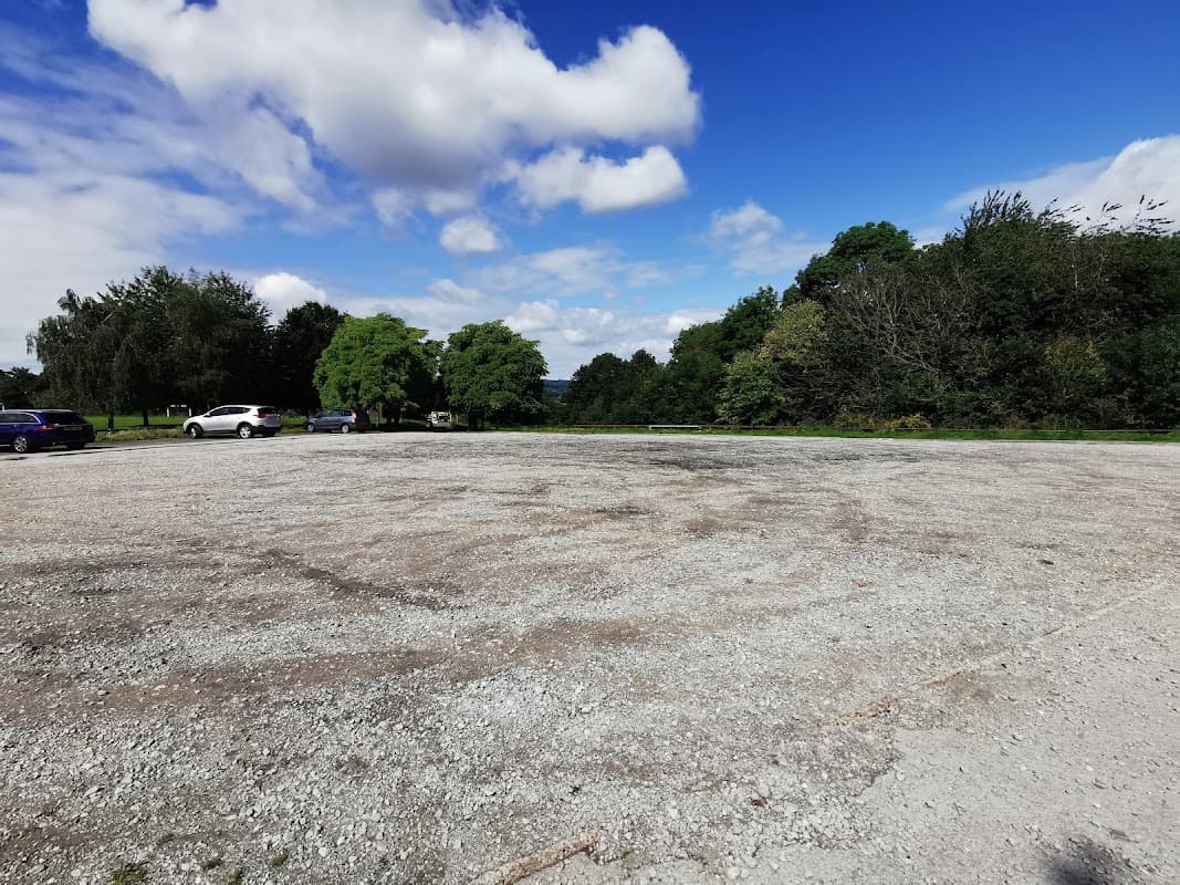 Gravel parking lot at Concord Park in Carbrook, Yorkshire, with scattered trees and a blue sky.