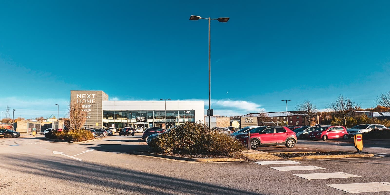 Next Parking lot with various parked cars, clear blue sky, and the Next Home store in the background.