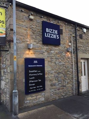 Bizzie Lizzie's restaurant sign on a stone building, featuring menus for breakfast, lunch, and dinner.
