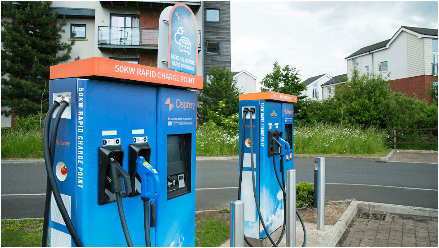 Two Osprey electric vehicle charging stations with hoses, surrounded by greenery and modern buildings in Carleton-in-Craven.