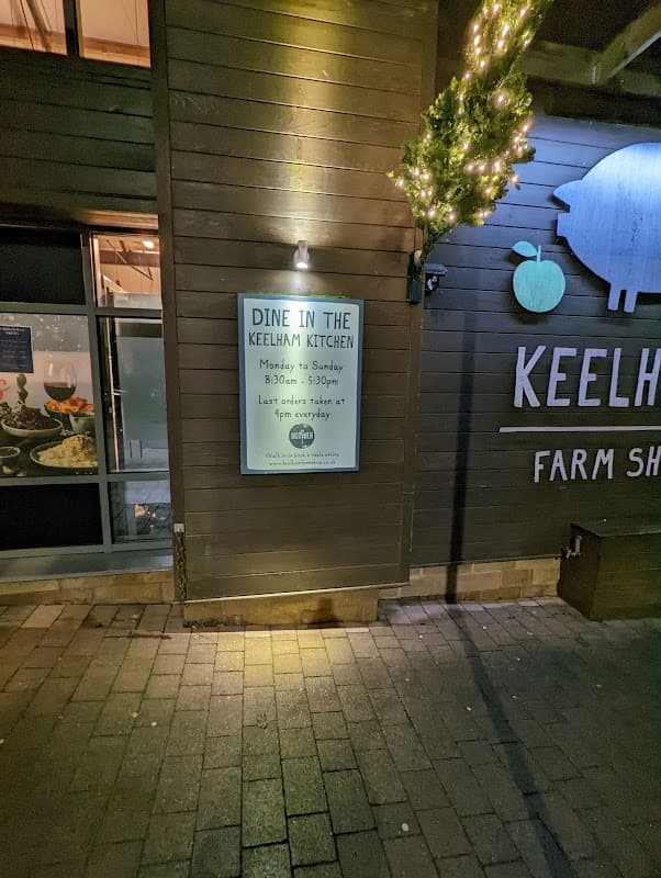 Sign for Keelham Kitchen, detailing hours and last order time, with festive lights on the exterior wall of the cafe.
