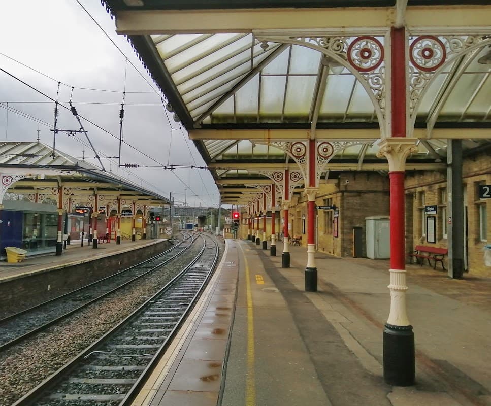 Victorian-style platform with ornate supports, railway tracks, and a cloudy sky at Skipton Railway Station.