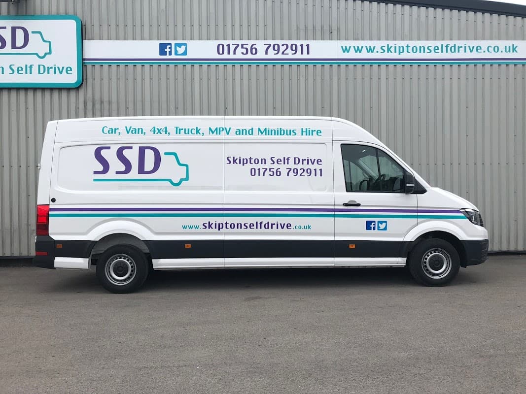 White van with "Skipton Self Drive" branding, contact details, and website, parked against a gray building.