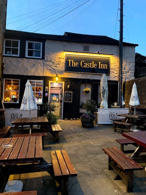 The Castle Inn, a charming bar with outdoor seating, illuminated sign, and flower pots, set in a quaint Yorkshire village.