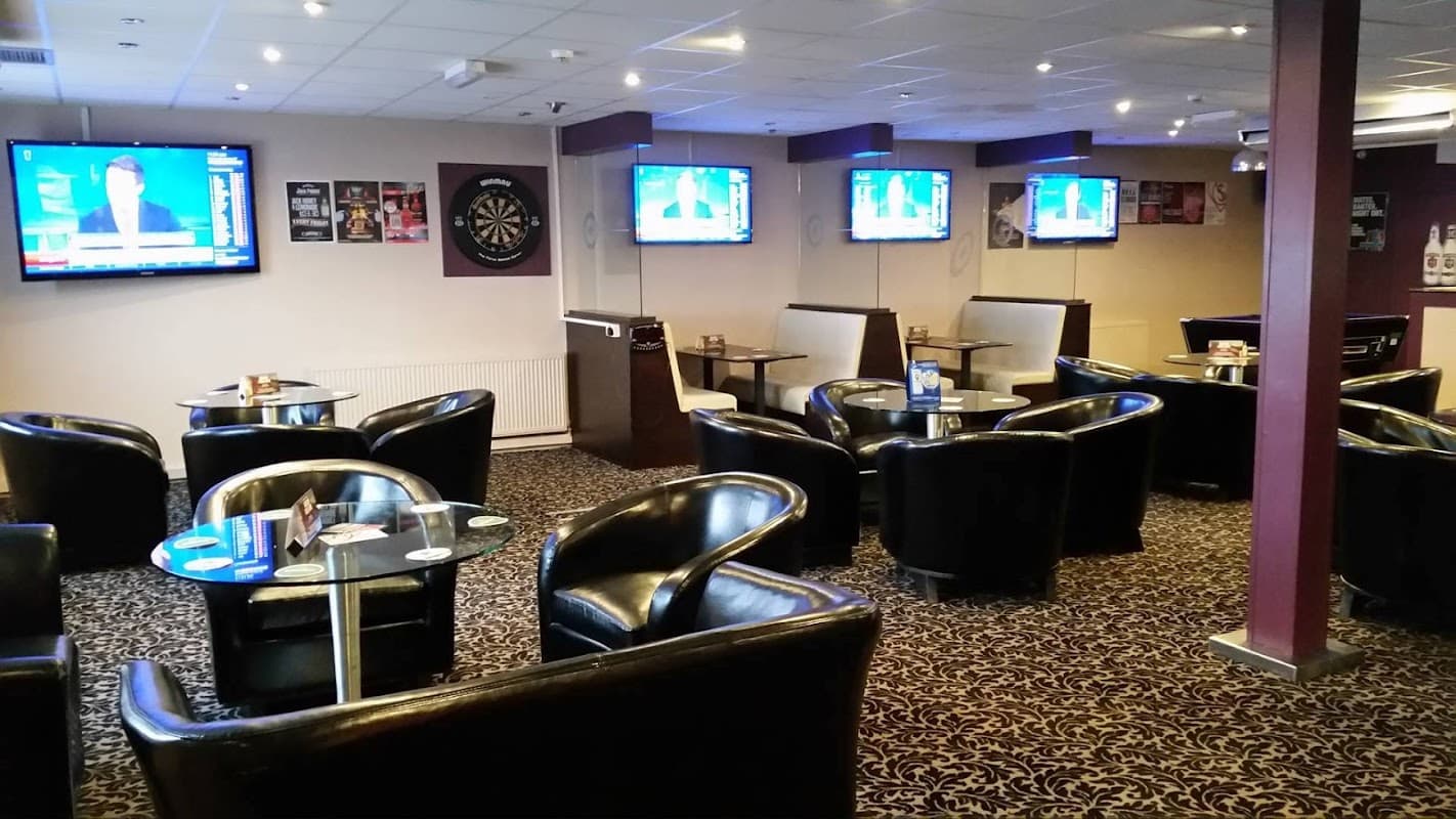 Cozy bar area with black leather chairs, tables, and multiple TVs displaying sports news in a relaxed atmosphere.