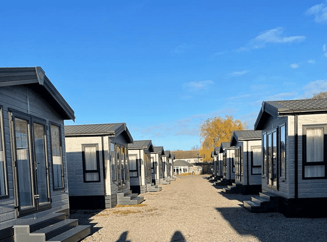 Row of holiday cabins at The Dog & Gun Holiday Park under a clear blue sky in Carlton Miniott, Yorkshire.