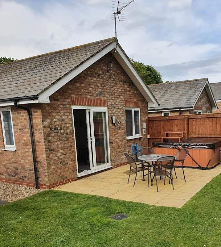 Bungalows with a patio area, outdoor seating, and a hot tub in a green space at Carnaby Covert Lane, Yorkshire.