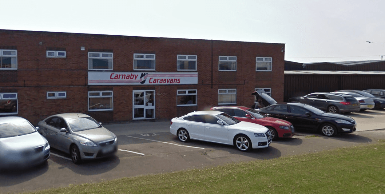 Carnaby Caravans Ltd building with a sign, parked cars, and a grassy area in front.
