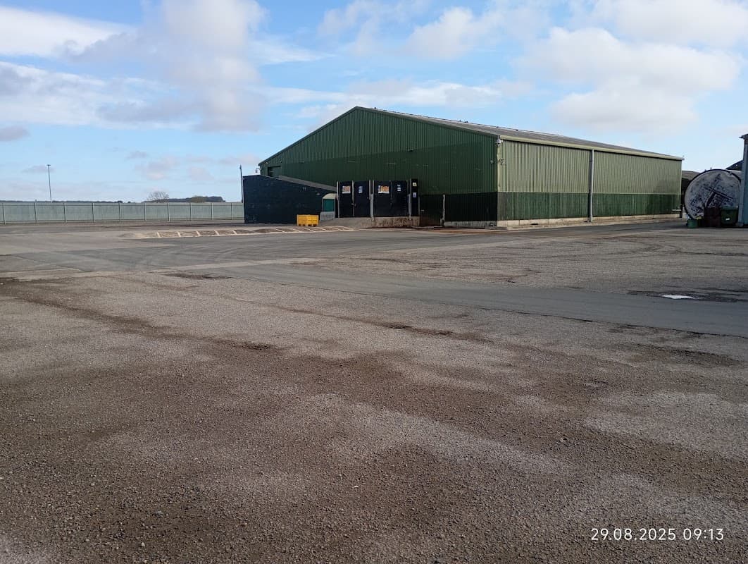 Large green warehouse building with a gravel parking lot and cloudy sky in the background.
