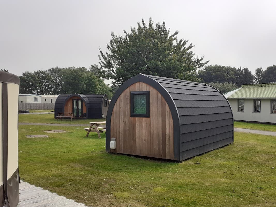 Wooden camping pods in a grassy area, surrounded by trees and other park facilities in Carnaby, Yorkshire.