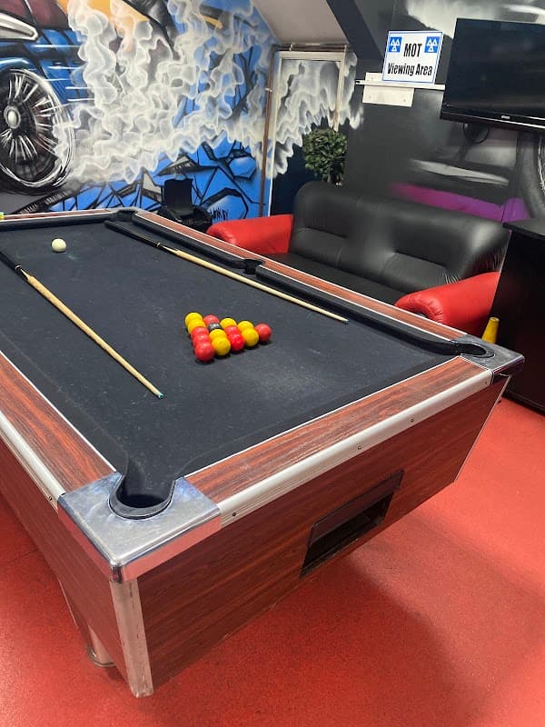 Pool table with colored balls arranged, red leather sofa, and a TV in a vibrant, modern garage setting.