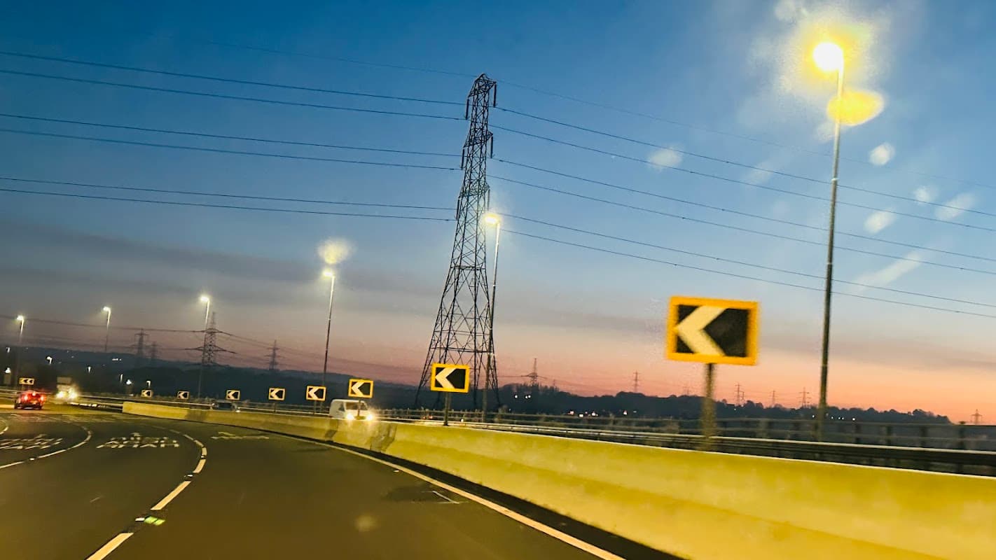 Motorcycle parking area with illuminated signs and power lines at dusk near a busy roadway in Catcliffe, Yorkshire.
