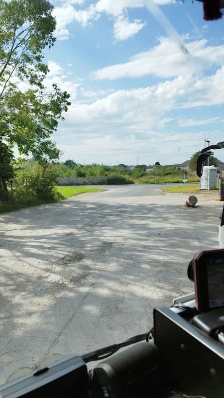 View of a wide, empty road leading into greenery under a bright blue sky with scattered clouds.