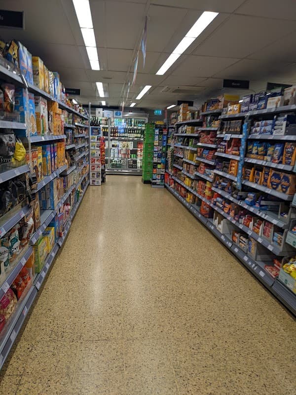 Aisle in a grocery store lined with shelves of various food products, leading to a checkout area in the background.