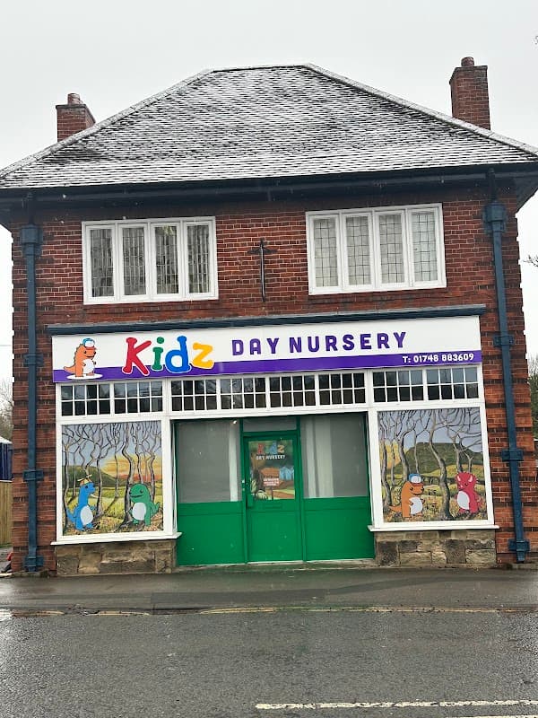 Brightly colored nursery sign with cartoon animals, large windows, and a green door in a brick building.