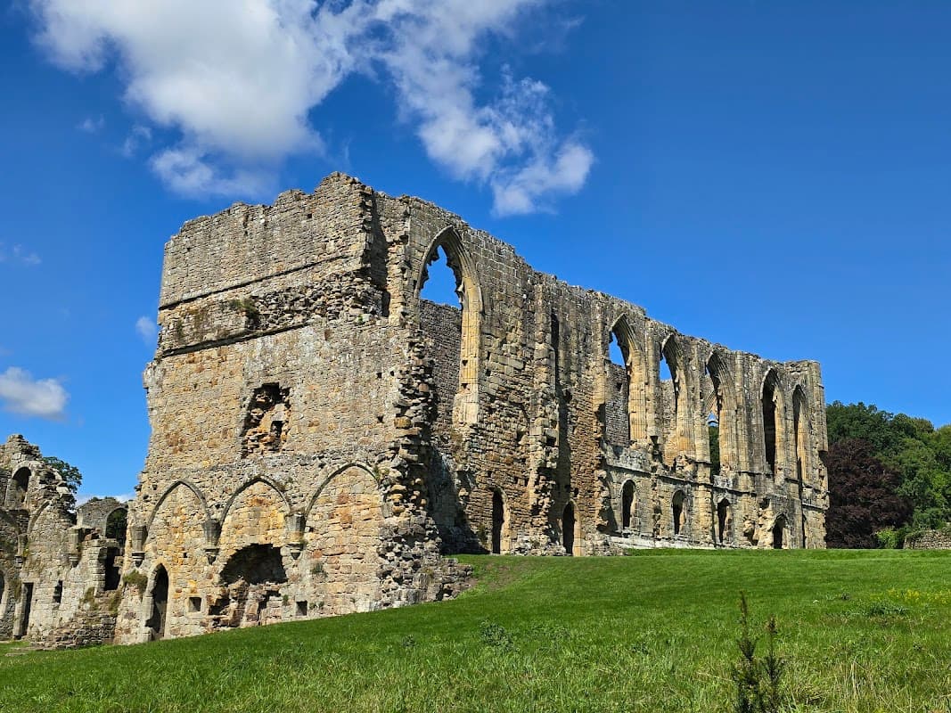 Ruins of St Agathaβs Church with arched windows, surrounded by green grass and blue sky in Easby, Yorkshire.