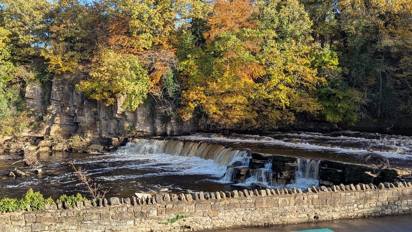 A cascading waterfall surrounded by autumn foliage and a stone wall in Catterick Garrison, Yorkshire.