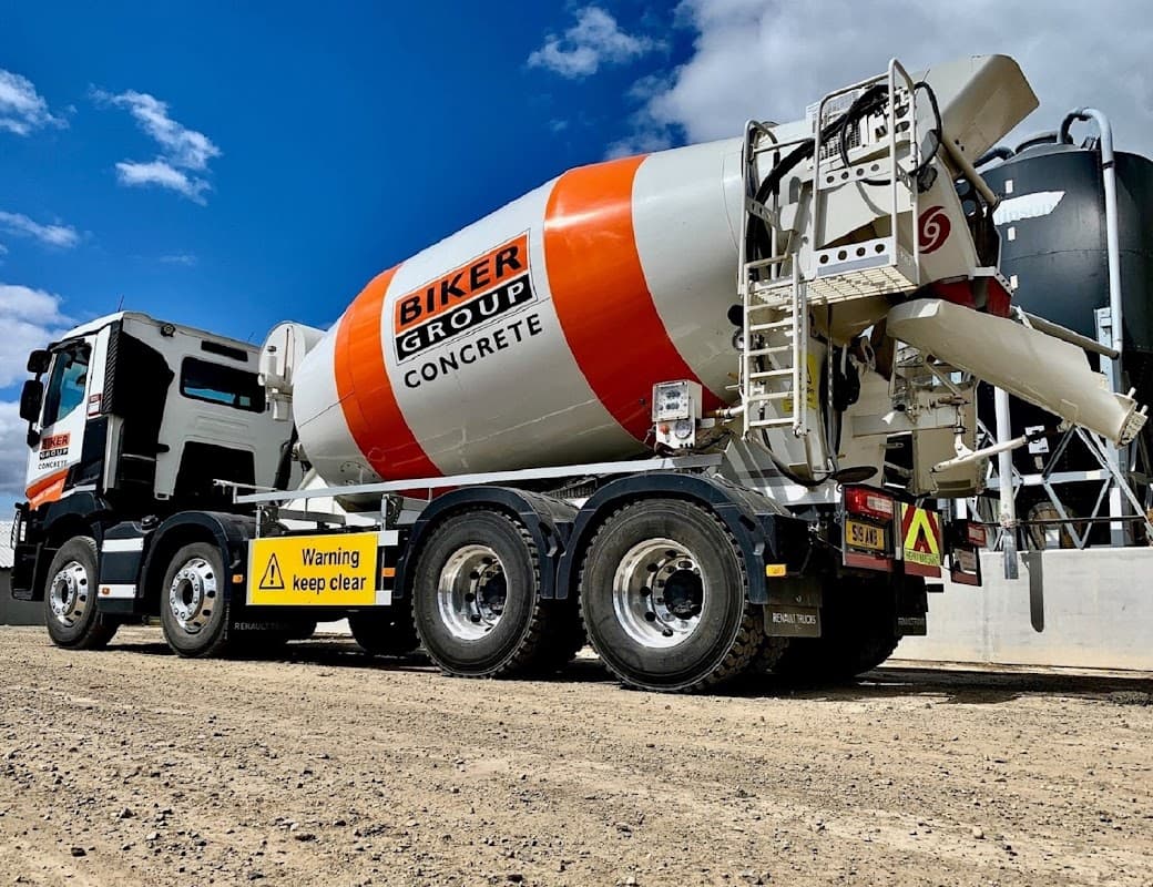 Concrete mixer truck with "Biker Group Concrete" branding, parked on gravel with warning signs visible.