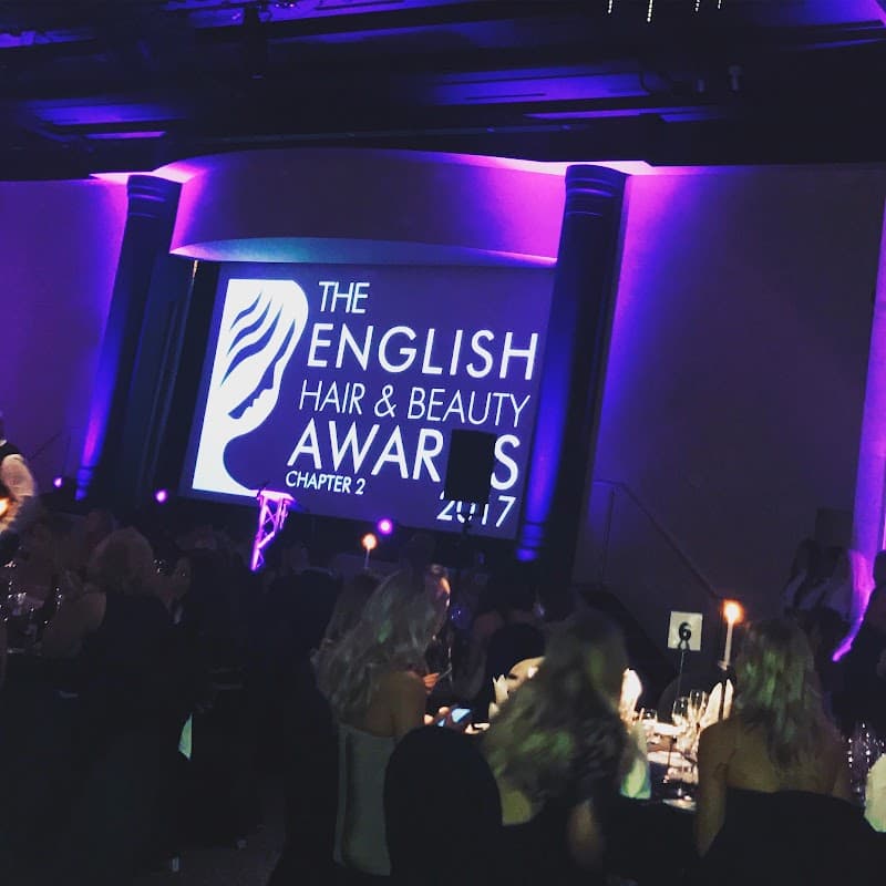 The English Hair & Beauty Awards 2017 displayed on a large screen, with a dimly lit venue and elegantly dressed attendees.