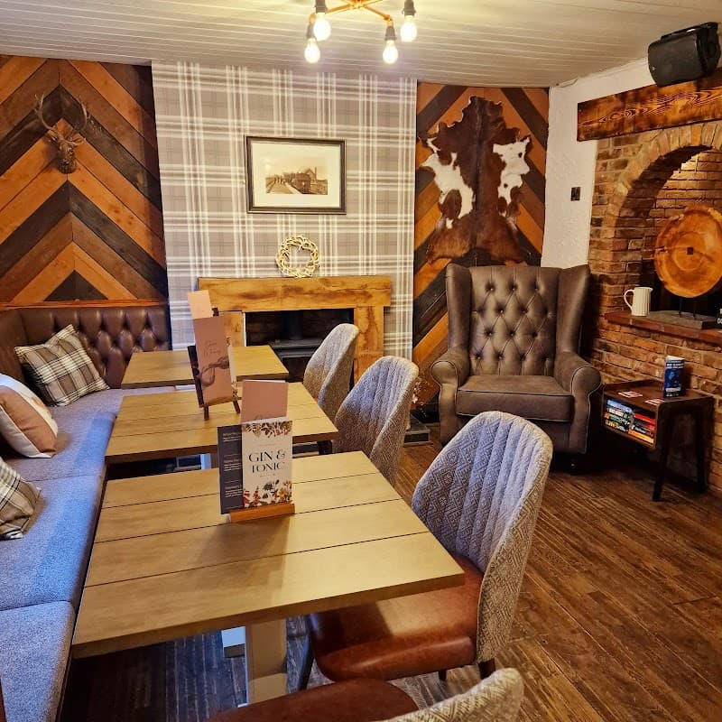 Cozy pub interior featuring wooden tables, plush chairs, and rustic decor with a fireplace and patterned walls.